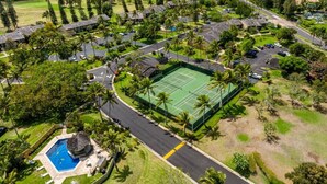 Vue aérienne d’un complexe hôtelier doté d’un court de tennis, d’une piscine et d’une végétation luxuriante.