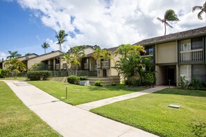 A row of two-story buildings with balconies, surrounded by well-maintained lawns and palm trees. - Spacious Family Condo Overlooking Golf Course (Kahuku)