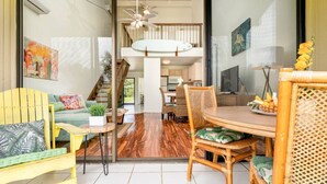Un vaste espace de vie comprenant une table à manger, des chaises et un canapé. Un escalier mène à l’étage supérieur.