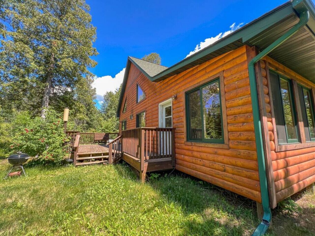 A log cabin with a deck, a grill, and a forested backdrop.