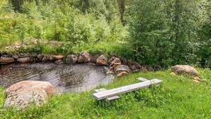 Rauhallinen ulkotila, jossa on pieni lampi, ja sitä ympäröivät kivet ja vehreä kasvillisuus.