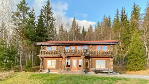 Kaksikerroksinen puinen mökki, jossa on parveke, ja sen ympärillä on metsää.