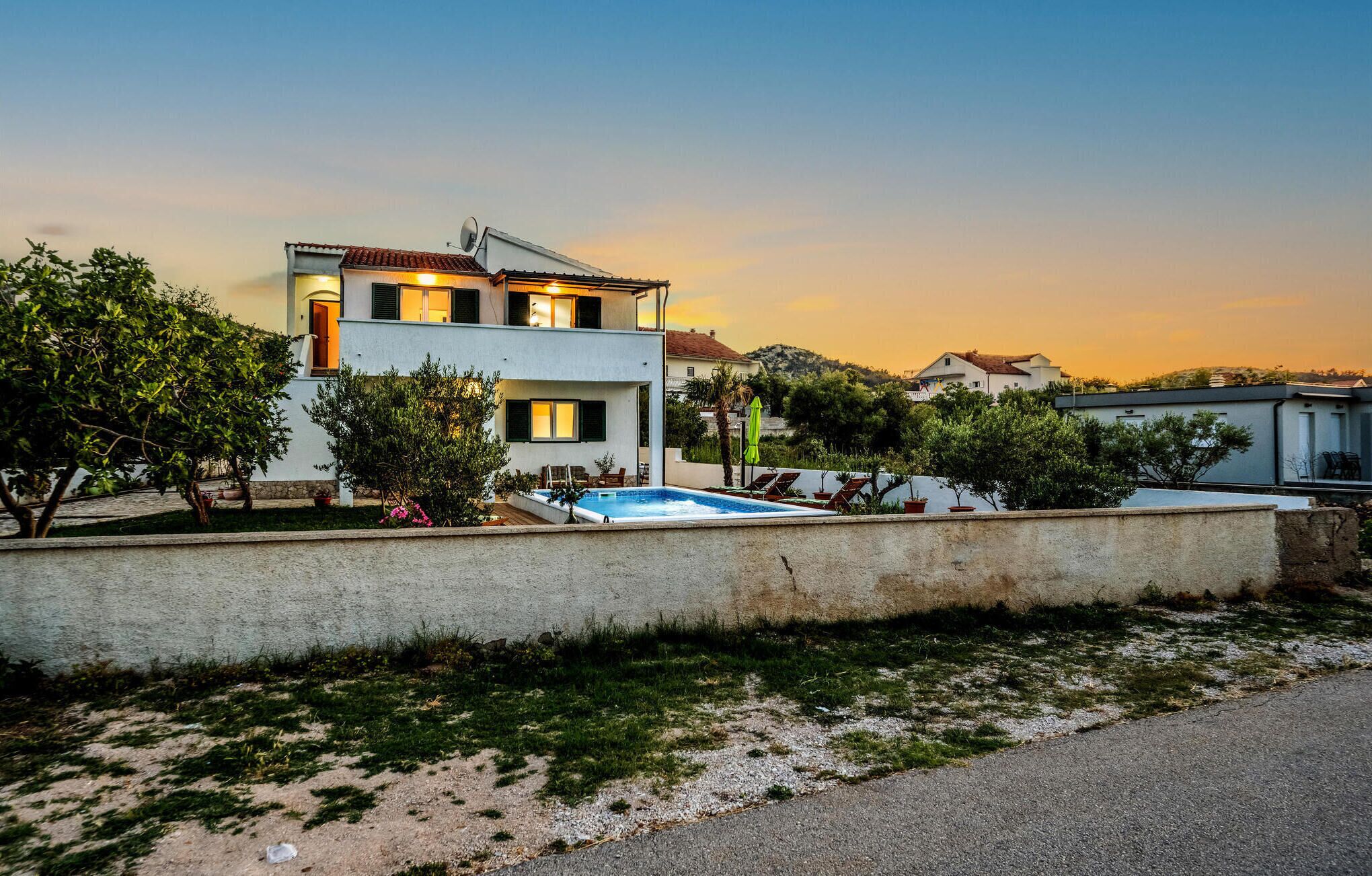 A modern two-story house with a swimming pool, surrounded by greenery and a clear sky.