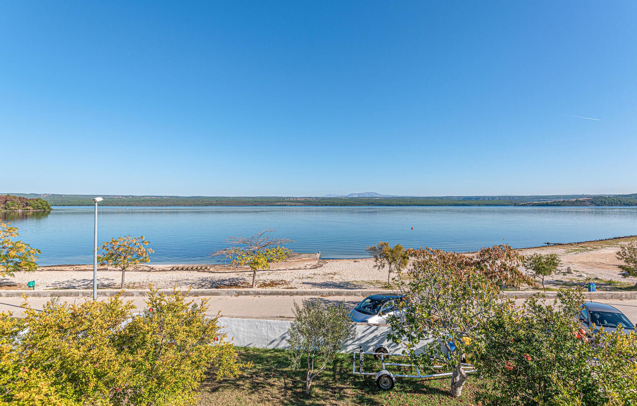 A parking area with a view of a calm lake, a clear sky, and some trees.