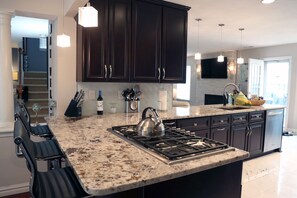 A kitchen with dark cabinets, a granite countertop, a gas stove, and hanging pendant lights. - Mai Villa-Hampton - Where good times happen! (Hampton)