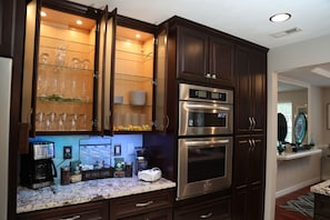 Una cocina con armarios de madera oscura, electrodomésticos de acero inoxidable y una vitrina con cristales que exhibe cristalería.