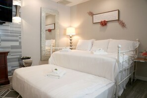 Quarto de hotel com uma cama grande, uma mesa de cabeceira, um espelho e um letreiro na parede.
