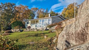 A modern house with a large glass window area, surrounded by a stone wall and a grassy lawn.