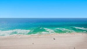 A wide beach with clear blue water and a few people walking along the shore. - 🏖️Lagoon Pool + Tiki Bar - 2BR Boardwalk 1810🏖️ (Panama City Beach)