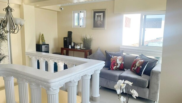 Amplia sala de estar con un sofá gris decorado con cojines con motivos navideños, una mesa de centro blanca con columnas clásicas y una araña.