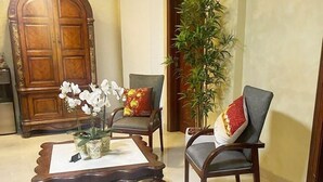Una sala de estar con una mesa de centro de madera, dos sillones, una planta en maceta y una puerta grande de madera.