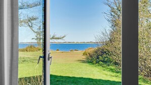 A view from a window overlooking a grassy area with a body of water and trees. - 3 bedroom cozy home in Spøttrup (Spøttrup)