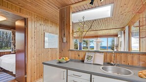 A wooden cabin interior with a kitchen, a bed, and a large window offering a view of the outdoors. - 3 bedroom cozy home in Spøttrup (Spøttrup)