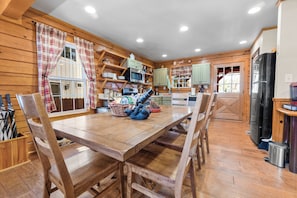 A wooden interior with a dining table, chairs, kitchen area, and a refrigerator.