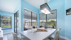 A bright dining area with a large table, white chairs, and a view of a pool and outdoor seating. - The Blue Lagoon of Naples (Naples)