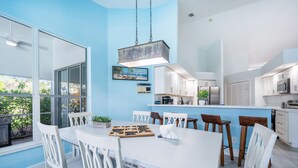A modern kitchen with white cabinets, a central island, and a dining area with white chairs and a table. - The Blue Lagoon of Naples (Naples)