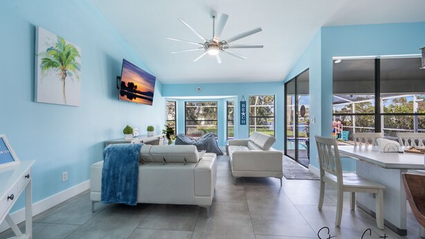 A spacious living room with a ceiling fan, two white sofas, a coffee table, and a TV. There is a large window with a view of the outdoors. - The Blue Lagoon of Naples (Naples)