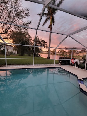 A pool with a clear view of a lake and surrounding trees during sunset.