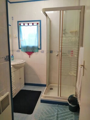 Baño con ducha, lavabo y ventana con cortina.
