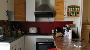 Una cocina compacta con horno empotrado, cocina a gas, cafetera y una pequeña isla con un taburete rojo.