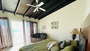 Ein Schlafzimmer mit Bett, Stuhl, Deckenventilator und einem fenster mit Vorhängen.