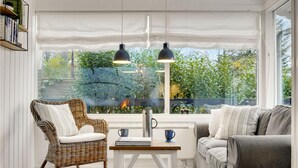 Une pièce chaleureuse avec un fauteuil en osier, un canapé gris et une table sur laquelle se trouvent un livre et une tasse.