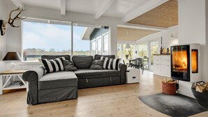Un salon moderne avec un canapé d’angle, une cheminée et de grandes fenêtres donnant sur l’extérieur.