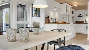 Une cuisine moderne avec des meubles blancs, un plan de travail en bois et un coin repas comprenant une table et des chaises.