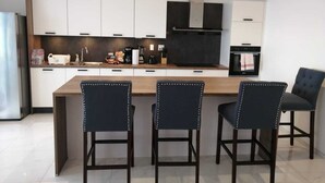 A modern kitchen with white cabinets, a central island with chairs, and a built-in oven. - Spectacular view of the Caribbean Sea (Sint Maarten)