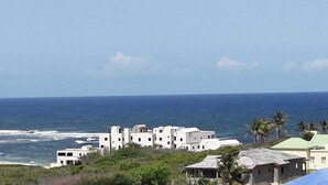 A coastal building complex with multiple structures, some with flat roofs and others with sloped roofs, overlooking the ocean. - Spectacular view of the Caribbean Sea (Sint Maarten)