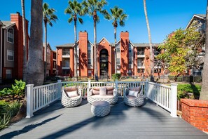 A building with brick facades, a white fence, and three wicker chairs on a deck.