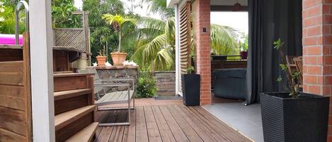 Une terrasse en bois avec des meubles d’extérieur, des plantes en pot et un mur en briques.