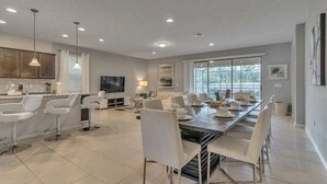 Un vaste espace dédié à la salle à manger, avec une longue table, des chaises blanches et des luminaires suspendus.