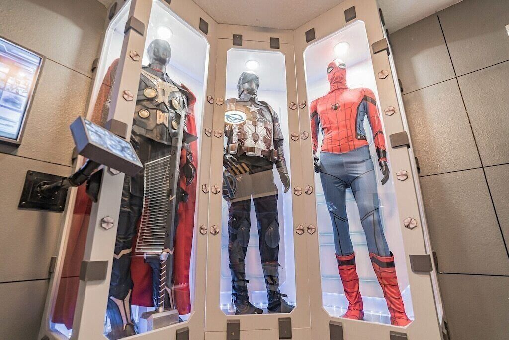 Trois mannequins sont exposés dans une vitrine, chacun portant un costume de super-héros différent.