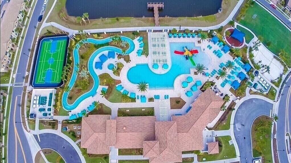 Vista aérea de un resort con una piscina grande, un tobogán de agua, una cancha de tenis y varias zonas de descanso.