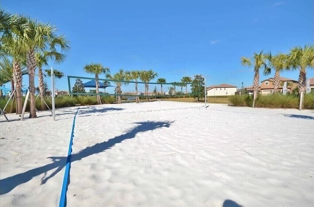 Una cancha de voleibol de playa con palmeras y casas al fondo.