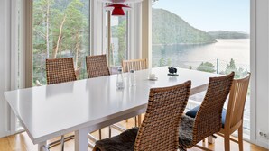 A dining area with a white table, wicker chairs, and a view of a lake and forest. - 4 bedroom nice home in Jørpeland (Jørpeland)