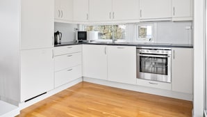 A modern kitchen with white cabinets, a stainless steel oven, and a window with a view of trees. - 4 bedroom nice home in Jørpeland (Jørpeland)