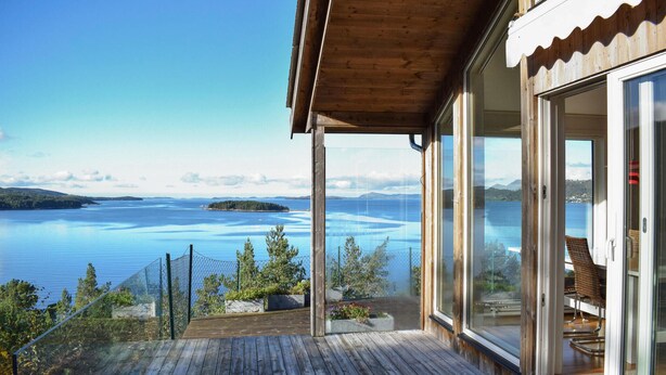 A wooden deck with a glass railing overlooking a large body of water and distant land. - 4 bedroom nice home in Jørpeland (Jørpeland)
