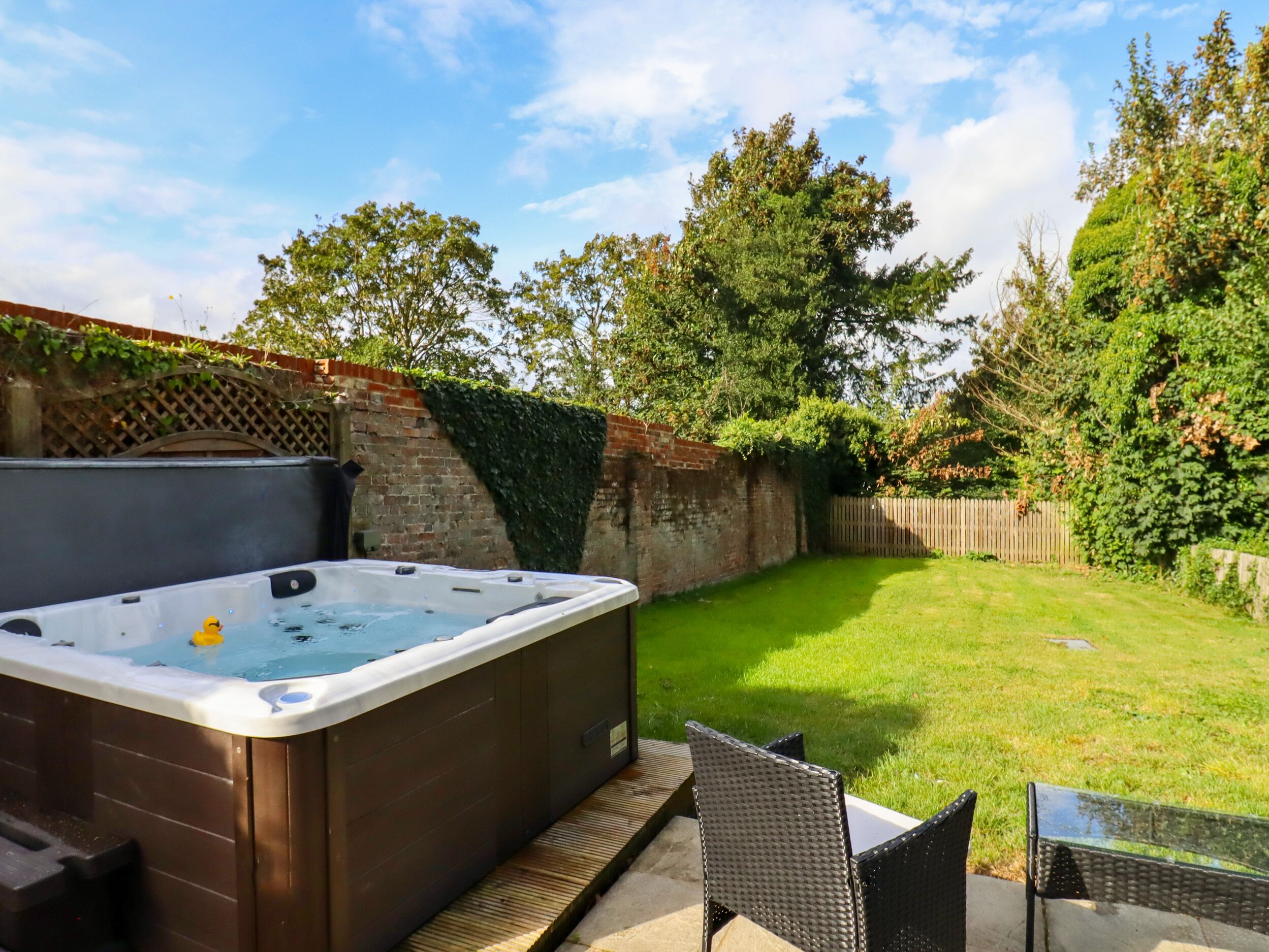 A hot tub in a backyard with a wooden deck, a brick wall, and a wooden fence.