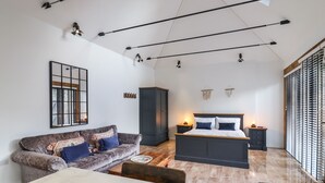 En moderne stue med sofa, spisebord, seng og et stort vindue med persienner.