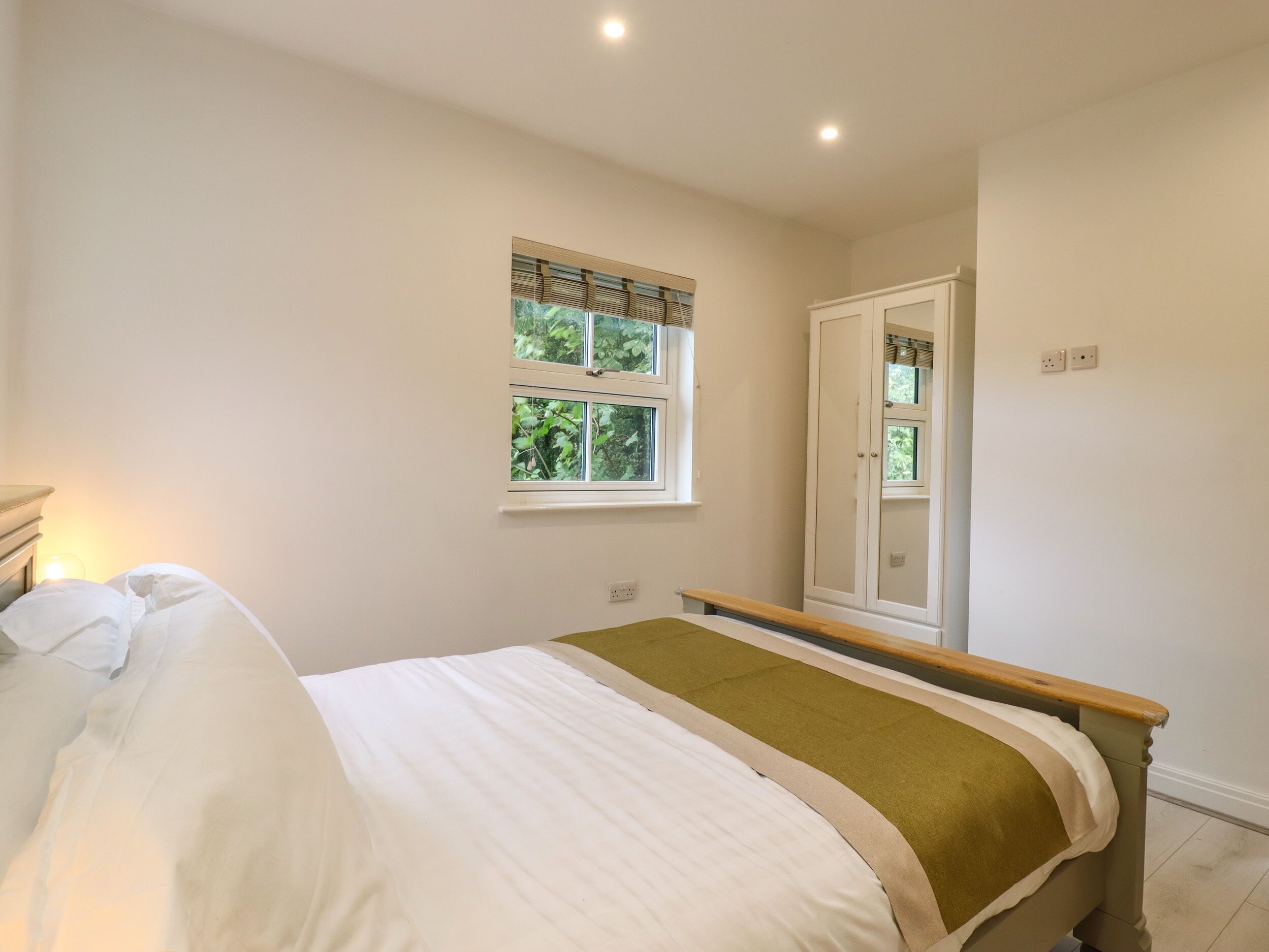 A bedroom with a bed, a window, a door, and a bedside table.