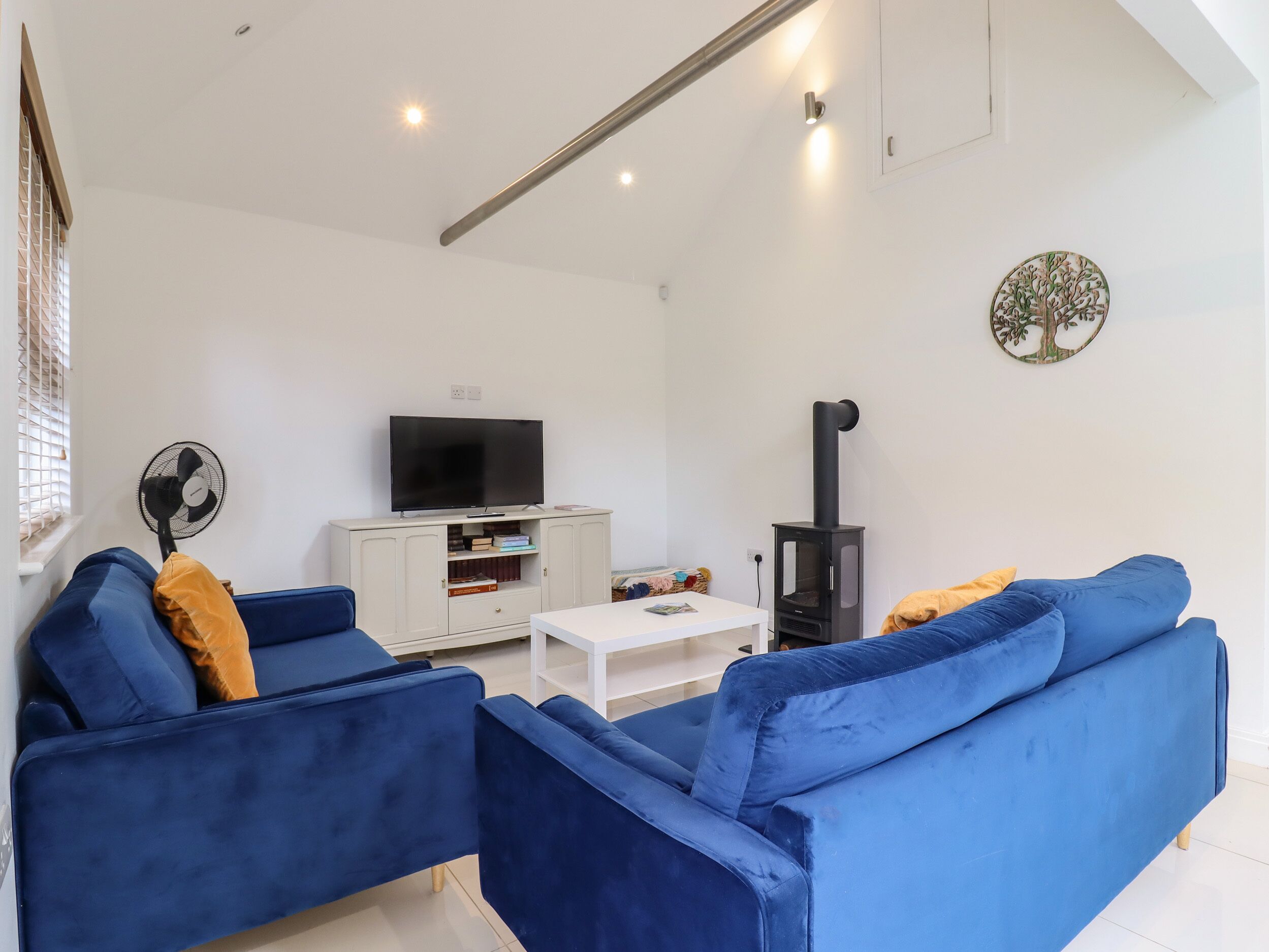 Una sala de estar moderna con un sofá azul, un mueble blanco para entretenimiento, un televisor negro y un estufa de leña.