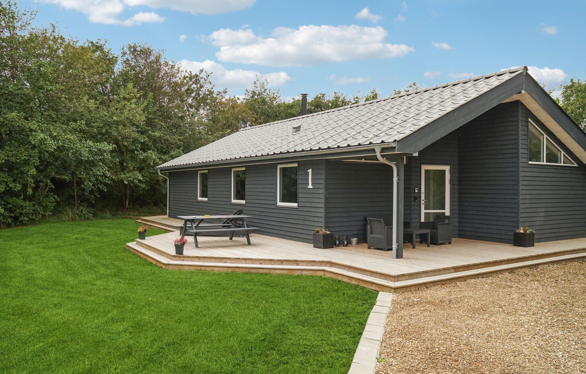 Et moderne hus med skråt tag, en overdækket terrasse med havemøbler og en velplejet græsplæne.