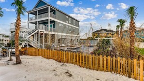 Una casa de playa de dos pisos con balcón, cerca viva de madera y palmeras.