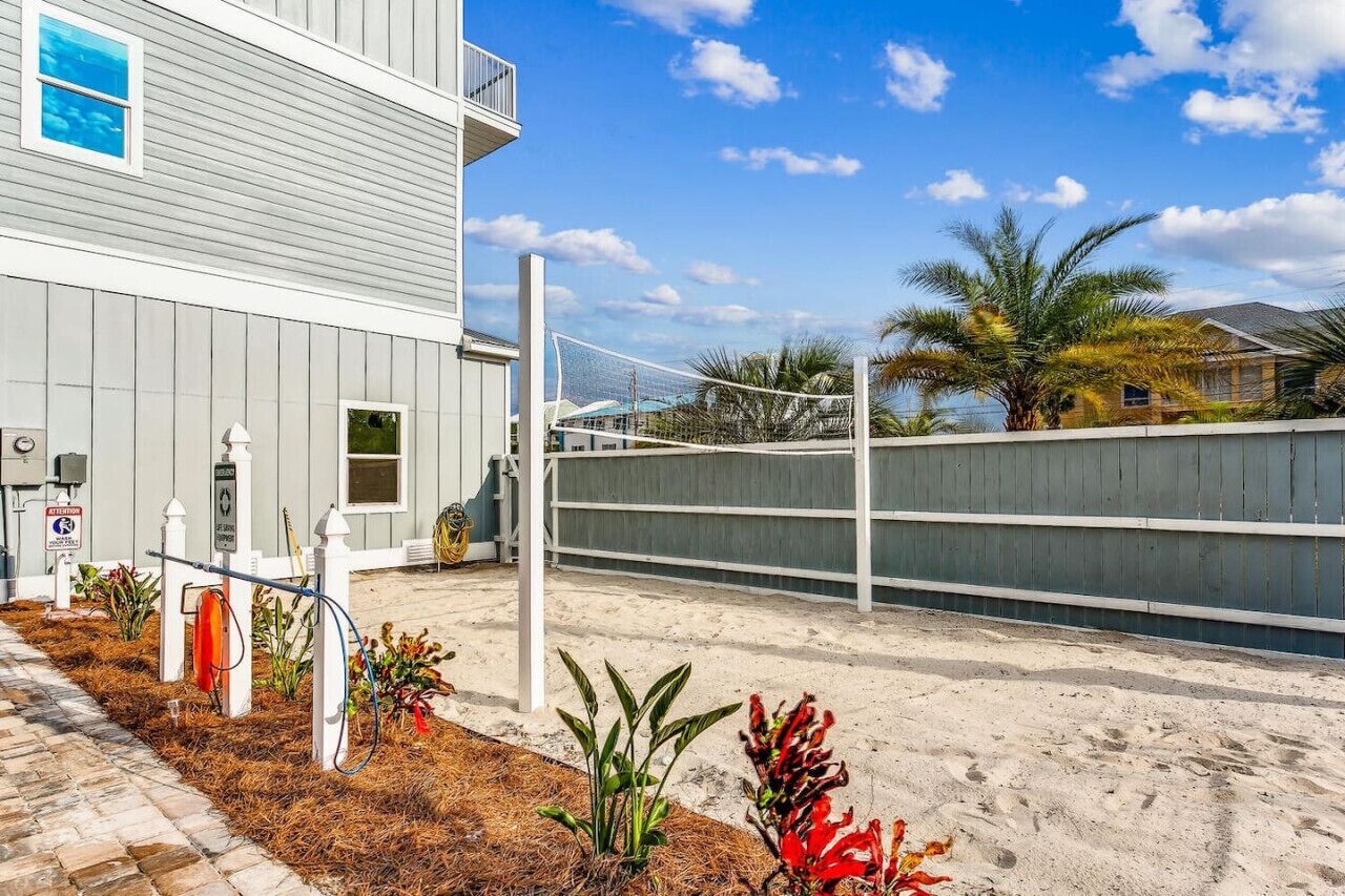 A modern building with a grey exterior, a white fence, and a sandy ground.