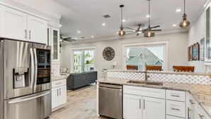 Una cocina moderna con electrodomésticos de acero inoxidable, armarios blancos y un amplio ventanal con vista a una casa.