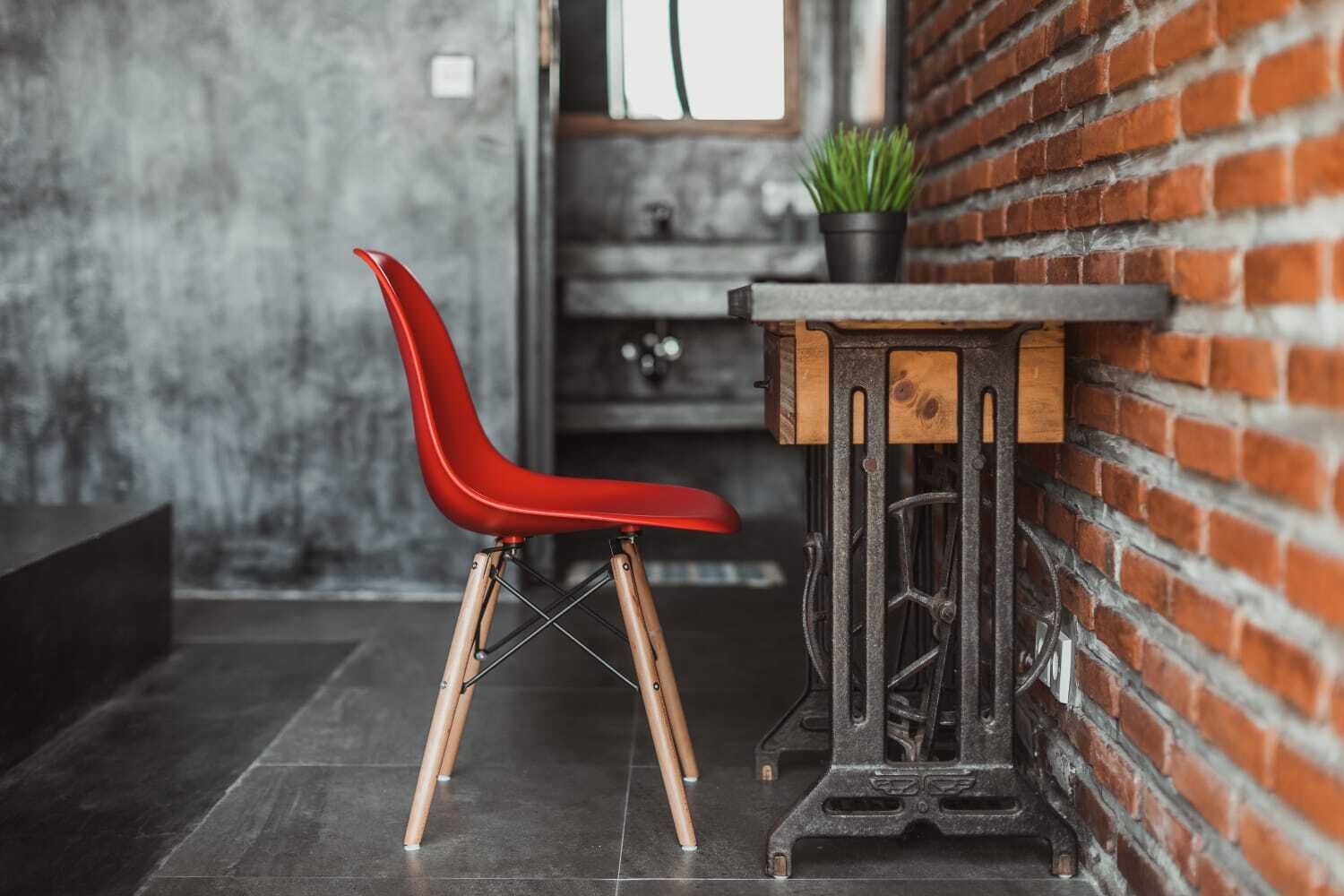 A red chair with wooden legs and a black metal table with a wooden top, placed against a brick wall.