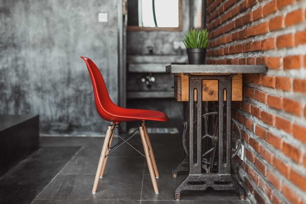 A red chair with wooden legs and a black metal table with a wooden top, placed against a brick wall.