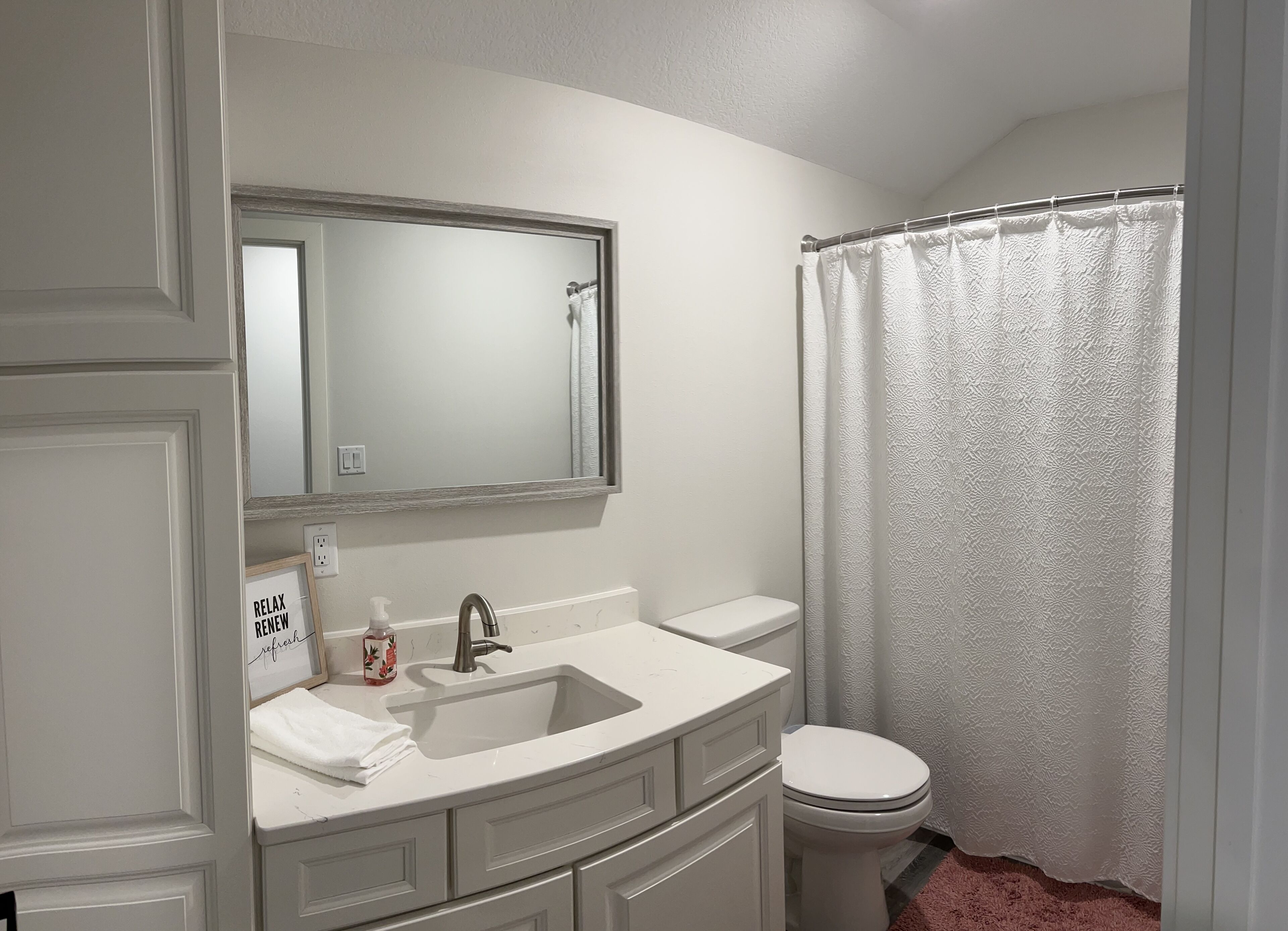 A bathroom with a white sink, mirror, and toilet, a shower curtain, and a towel on the sink.
